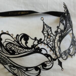 Elegant black masquerade mask with rhinestones resting on white fabric.