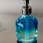 Blue glass soap dispenser with metal pump sitting on a reflective surface.