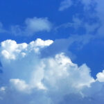 Large white cumulus clouds rising against a bright blue sky.