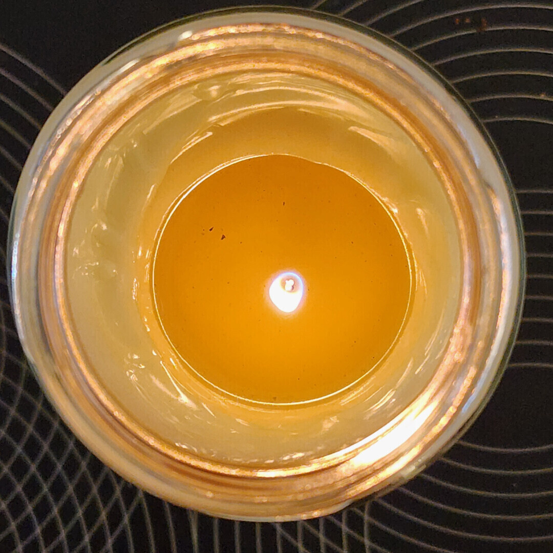 Top view of candle flame inside a glass jar with warm light glow and circular reflections on dark background