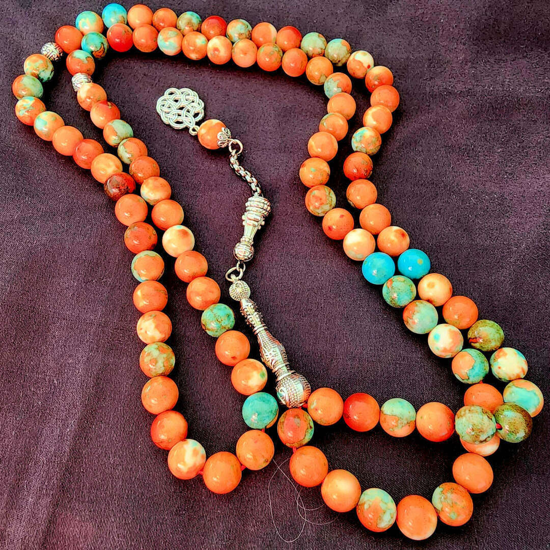 Colorful orange and turquoise prayer beads arranged on a dark background in a still life composition.