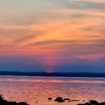 Colorful sunset clouds fading over a calm lake with rocks and birds in the water.