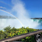 Rainbow forming in the mist above Niagara Falls with cascading waterfall and river below.