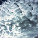 Textured gray clouds filling the sky with sunlight glowing behind them.