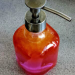 A glass soap dispenser filled with orange and pink liquid showing colour gradients and reflections.