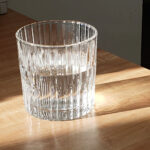 Glass of water on a wooden table with sunlight creating reflections and shadows.