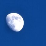 A half moon visible against a clear blue daytime sky.