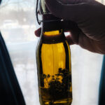 Glass bottle filled with olive oil infused with thyme and garlic held near a window in natural light