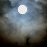 A bright moon surrounded by soft clouds creating a glowing atmospheric effect.