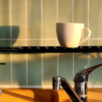 Coffee cup on a rack above a kitchen sink illuminated by warm sunlight.