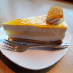 Slice of cheesecake with orange topping served on a white plate with a fork.