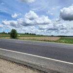 Wide rural farmland landscape beside a country road under dramatic cloud formations.
