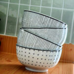 Stack of ceramic bowls with minimalist patterns placed on a wooden countertop.