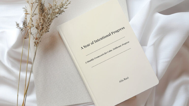 A Year of Intentional Progress book styled on soft white fabric beside a notebook and dried stems