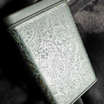 Decorative metal box with intricate engraved pattern resting on soft fabric, partially illuminated by soft light