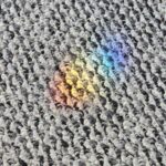 Small rainbow light reflection on a textured woven fabric surface with visible pattern detail
