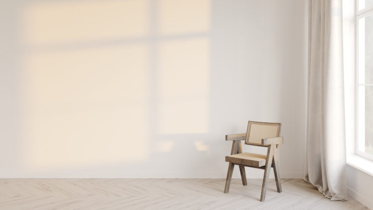 Soft natural light casting a window shadow on a plain wall beside a single chair in a quiet, minimal room
