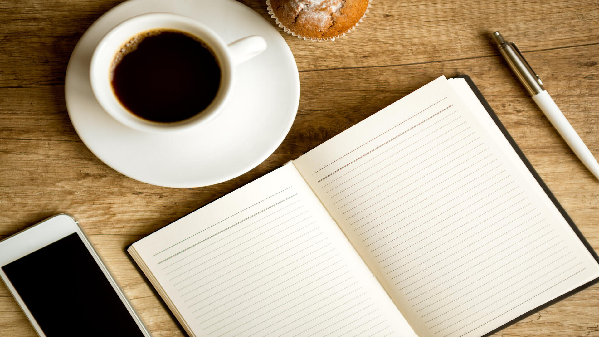 Open notebook beside a cup of coffee, smartphone, and pen on a wooden desk, representing business planning and sustainable growth.