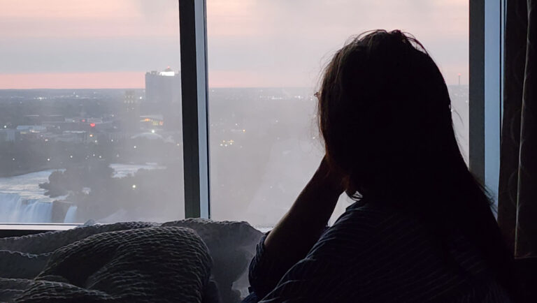 Silhouette of a woman sitting by a window overlooking Niagara Falls at dusk.