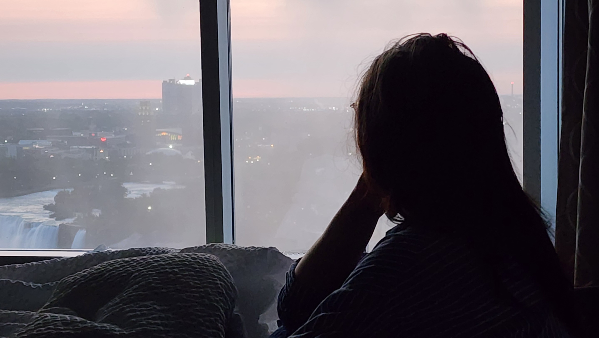 Silhouette of a woman sitting by a window overlooking Niagara Falls at dusk.