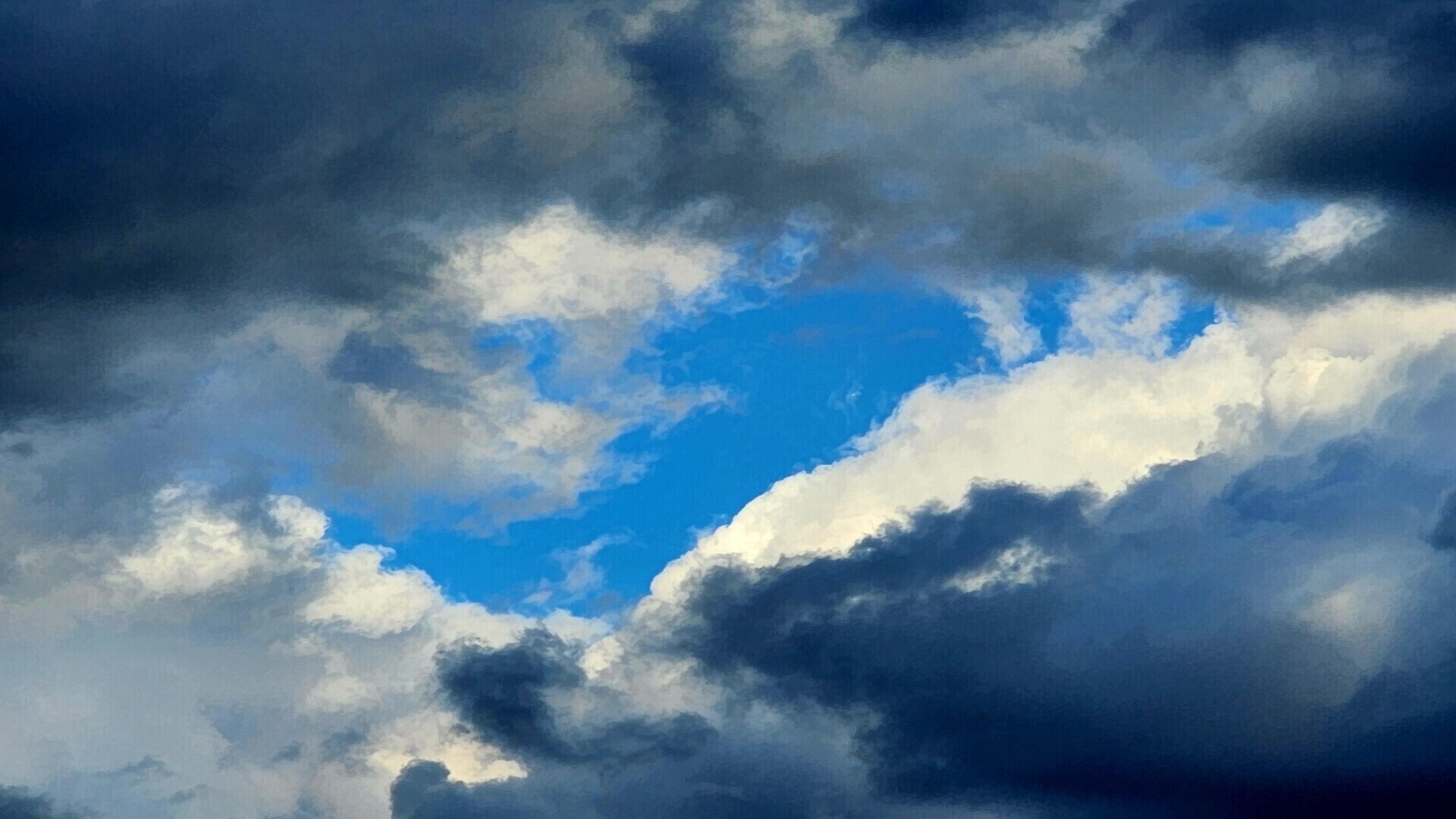 Dramatic white and dark blue clouds frame a bright opening of blue sky.